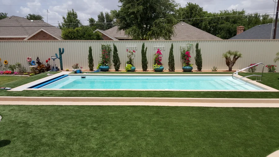 A backyard pool framed by lawn and flowering plants